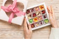 Female hands with delicious candies in box on color background