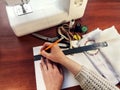 Female hands draw with a pencil and a ruler on white paper against the background of a sewing machine and accessories, close-up. Royalty Free Stock Photo