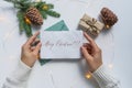 Female hands, dressed in a white sweater, hold a sheet of white paper with the inscription Merry Christmas. The concept of gifts f