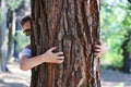 Female hands embrace tree, and her face looks from behind him