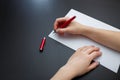 Female hands with fir-tree forest manicure holding red pen over white paper on black background. Christmas or winter nail art. Royalty Free Stock Photo