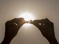 Female hands fit together two pieces of a puzzle with the setting sun in the background Royalty Free Stock Photo