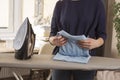 Female hands fold a ironed T-shirt lying on an ironing board. The iron stands on a foot on an ironing board. Household duties.