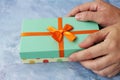 Female hands giving a wrapped Christmas or other holiday handmade gift with orange ribbon