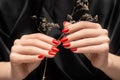 Female hands with glitter red nail design. Female hands hold autumn flower. Woman hands on black fabric background Royalty Free Stock Photo