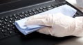 Female hands in gloves disinfecting laptop keyboard using wet disinfectant wipes. Woman cleaning keyboard. New Normal cleaning