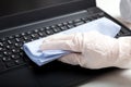 Female hands in gloves disinfecting laptop keyboard using wet disinfectant wipes. Woman cleaning keyboard from viruses bacteria