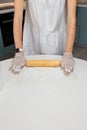 Female hands in gloves roll out mastic with rolling pin to make decor for cupcakes, white table background