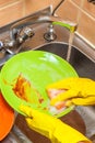 female hands in gloves wash a green plate in the sink in the kitchen Royalty Free Stock Photo