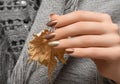 Female hands with gold nail design. Red nail polish manicured hands. Woman hands hold yellow autumn leaf