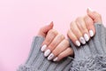 Female hands in gray knitted sweater with beautiful manicure - white ivory nails with flower on pink paper background with copy