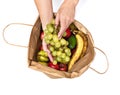 Female hands hold a bunch of green grapes, taking it out of a paper bag full of different fruits, isolated on a white background. Royalty Free Stock Photo