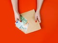 Female hands hold craft envelope with Euro, money on red table. Top view Royalty Free Stock Photo