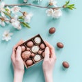 Female hands hold gift box of chocolate Easter eggs on turquoise background