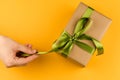 Female hands hold a gift box wrapped in craft paper and tied with a green ribbon on a yellow background close-up Royalty Free Stock Photo