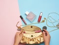 Female hands hold a golden clutch bag with various cosmetics and jewelry on a blue background Royalty Free Stock Photo