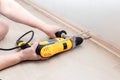 Female hands hold a heavy drill tool and make a hole in the wall for attaching the baseboard Royalty Free Stock Photo