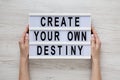 Female hands hold a lightbox with `Create your own destiny` words over white wooden background, top view. Overhead, from above, Royalty Free Stock Photo