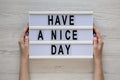 Female hands hold a lightbox with `Have a nice day` words on a white wooden background, top view. Overhead, from above, flat lay Royalty Free Stock Photo