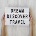 Female hands hold lightbox with text `Dream Discover Travel` over white wooden background, overhead view. From above, flat lay, Royalty Free Stock Photo