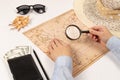 Female hands hold a magnifying glass over the world map. on a white wooden table lies a black wallet with money, a straw hat, a sh Royalty Free Stock Photo