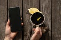 Female hands hold a mobile phone and a cup of tea with lemon on an old wooden table Royalty Free Stock Photo