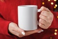 Female hands hold a mockup white tea mug in a red winter sweater, gold bokeh Royalty Free Stock Photo