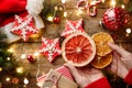 Female hands hold slice of orange over wooden background with Christmas gingerbread cookies, fir branches, decorations, lights Royalty Free Stock Photo