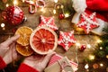 Female hands hold slice of orange over wooden background with Christmas gingerbread cookies, fir branches, decorations, lights Royalty Free Stock Photo