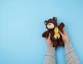 Female hands hold a small brown teddy bear which holds in its paw a yellow ribbon Royalty Free Stock Photo