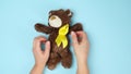 Female hands hold a small teddy bear with a yellow ribbon folded in a loop on a blue background