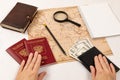 Female hands hold two passports and a black leather wallet with money. on a white wooden table lies a map of the world, a magnifyi