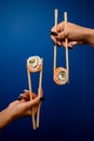 Female hands hold vertical sushi rolls with chopsticks on a blue background Royalty Free Stock Photo