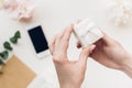 Female hands hold white gift box on background of flowers and phone. top view Royalty Free Stock Photo