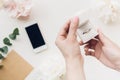 Female hands hold white gift box on background of flowers and phone. top view Royalty Free Stock Photo