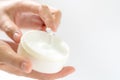 Female hands holding and apply jar of nourishing cream on white background.Skin care and beauty concept.Closeup