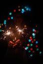 Female hands holding bengal lights on black background with blurry colored lights. Christmas and new year Royalty Free Stock Photo