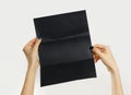 Female hands holding a black booklet triple sheet of paper. Isolated on gray background. Closeup