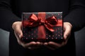 female hands holding a black gift box with a red bow made of satin ribbon, Generative AI Royalty Free Stock Photo