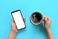 Female hands holding black mobile phone with blank white screen and mug of coffee. Mockup image with copy space. Top view on blue Royalty Free Stock Photo