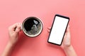 Female hands holding black mobile phone with blank white screen and mug of coffee. Mockup image with copy space. Top view on pink Royalty Free Stock Photo