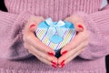 Female hands holding a blue gift box in heart shape and pink woolen sweater in background Royalty Free Stock Photo