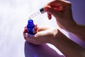 Female hands is holding blue glass bottle and pipette full of cosmetic serum for skin care treatment.