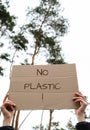 Female hands holding cardboard with text NO PLASTIC outdoors. Nature background. Protester activist