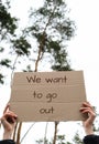 Female hands holding cardboard with text WE WANT TO GO OUT outdoors. Nature background. Protester activist