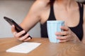 Female hands holding cell phone and a cup of coofee on the wooden table