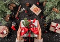 Female hands holding Christmas gift box with red ribbon on holiday background with Fir branches, pine cones Royalty Free Stock Photo