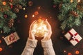 Female hands holding Christmas glowing ball on holiday background with Fir branches, gifts. Royalty Free Stock Photo