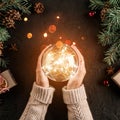 Female hands holding Christmas glowing ball on holiday background with Fir branches, gifts. Royalty Free Stock Photo