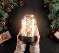 Female hands holding Christmas glowing ball on holiday background with Fir branches, gifts. Xmas and Happy New Year card, bokeh,